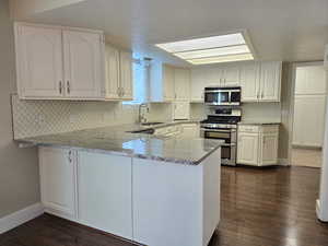 Kitchen featuring light stone countertops, a peninsula, white cabinetry, a sink, and stainless steel appliances