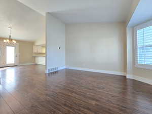 Unfurnished living room featuring a chandelier, a wealth of natural light, visible vents, and dark wood-style floors
