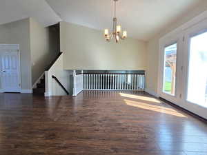 Interior space featuring an inviting chandelier, visible vents, vaulted ceiling, wood finished floors, and baseboards