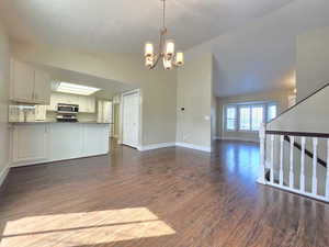 Unfurnished living room featuring baseboards, a sink, dark wood-style flooring, a chandelier, and high vaulted ceiling