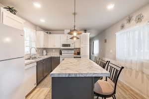 Kitchen featuring a center island, a sink, light countertops, white appliances, and white cabinetry