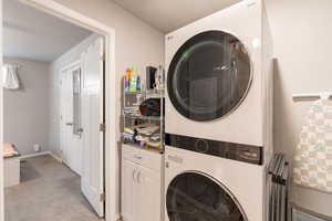Laundry area featuring light carpet, stacked washer / drying machine, baseboards, and cabinet space