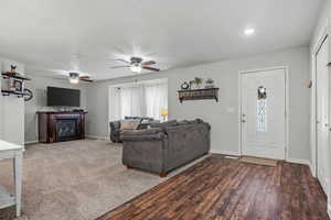 Living area with a glass covered fireplace, baseboards, recessed lighting, ceiling fan, and wood finished floors