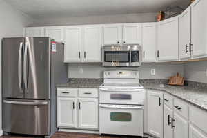 Kitchen with light stone counters, dark wood finished floors, white cabinets, and stainless steel appliances