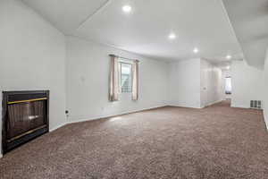 Unfurnished living room featuring a glass covered fireplace, carpet flooring, visible vents, and baseboards