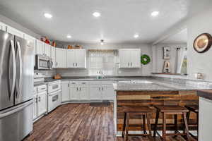 Kitchen featuring a healthy amount of sunlight, white cabinets, a kitchen bar, and appliances with stainless steel finishes