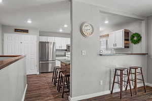 Kitchen featuring a breakfast bar, baseboards, white cabinets, dark wood-type flooring, and appliances with stainless steel finishes