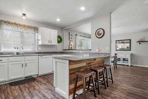 Kitchen featuring white cabinets, a sink, white dishwasher, a breakfast bar area, and dark wood-style floors