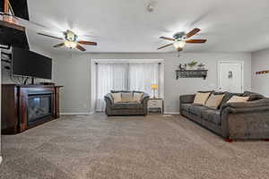 Living area featuring a glass covered fireplace, carpet, baseboards, and a ceiling fan