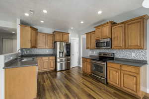 Kitchen featuring dark wood finished floors, brown cabinetry, dark countertops, a sink, and stainless steel appliances
