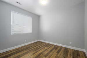 Unfurnished room featuring dark wood-type flooring, visible vents, and baseboards