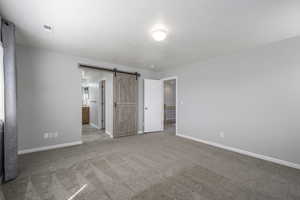 Unfurnished bedroom with carpet floors, baseboards, a barn door, and visible vents