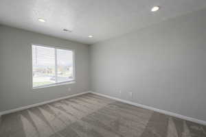 Carpeted spare room with a textured ceiling, baseboards, visible vents, and recessed lighting