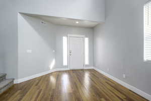Entrance foyer with dark wood-type flooring, visible vents, baseboards, and stairway