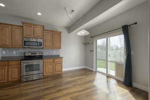 Kitchen featuring stainless steel appliances, brown cabinetry, backsplash, and dark countertops