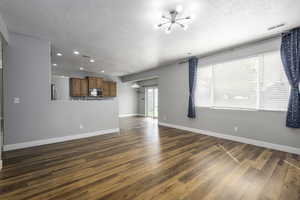 Unfurnished living room with baseboards, a chandelier, recessed lighting, a textured ceiling, and dark wood-type flooring