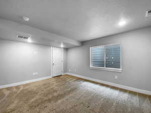 Finished basement with carpet, visible vents, a textured ceiling, and baseboards