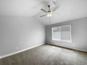 Carpeted spare room with visible vents, ceiling fan, baseboards, and lofted ceiling