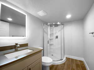 Full bath featuring a shower stall, a textured ceiling, wood finished floors, and toilet