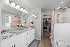 Bathroom featuring curtained shower, wood finished floors, double vanity, and a sink