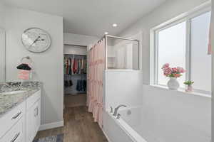 Bathroom with a walk in closet, a shower stall, vanity, wood finished floors, and a garden tub