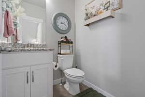 Half bathroom featuring toilet, vanity, wood finished floors, and baseboards