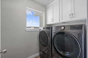 Clothes washing area featuring separate washer and dryer, baseboards, and cabinet space