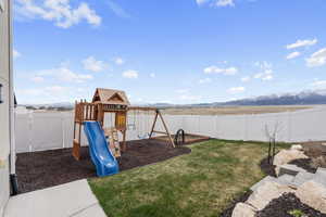 View of jungle gym featuring a fenced backyard, a mountain view, and a lawn