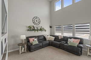 Living room featuring light colored carpet, baseboards, and a towering ceiling