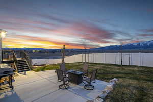 Patio terrace at dusk with a lawn, a fenced backyard, a fire pit, and stairs