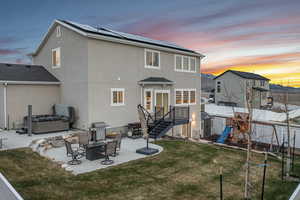 Back of property at dusk featuring a patio, a fenced backyard, a hot tub, and a lawn