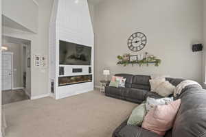 Carpeted living area with a towering ceiling, a glass covered fireplace, and baseboards