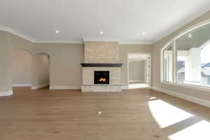 Unfurnished living room with baseboards, ornamental molding, a fireplace, light wood-style flooring, and arched walkways