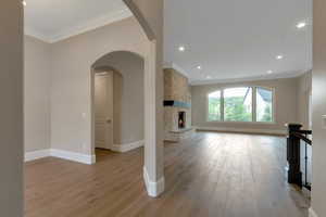 Unfurnished living room featuring baseboards, recessed lighting, a fireplace, crown molding, and light wood-style floors