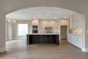 Kitchen featuring stainless steel appliances, arched walkways, white cabinets, and light countertops