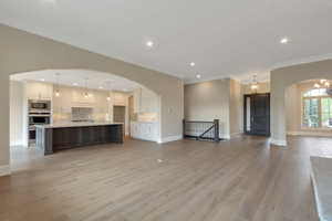 Unfurnished living room with baseboards, arched walkways, light wood-type flooring, and crown molding