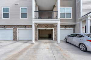 Exterior space with an attached garage, driveway, stone siding, and a balcony