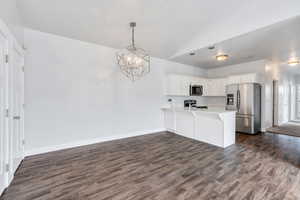 Kitchen featuring an inviting chandelier, dark wood finished floors, a peninsula, light countertops, and stainless steel appliances