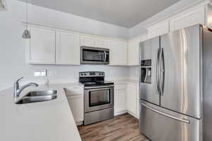 Kitchen featuring white cabinetry, dark wood-style flooring, a sink, hanging light fixtures, and stainless steel appliances