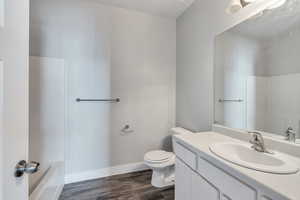 Full bath featuring baseboards, toilet, a tub to relax in, vanity, and wood finished floors