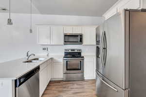 Kitchen featuring light wood-style floors, visible vents, appliances with stainless steel finishes, light countertops, and a sink