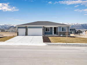 View of front of house with a garage, a front yard, stone siding, a mountain view, and concrete driveway