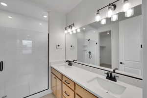 Full bath with a stall shower, double vanity, a sink, and recessed lighting