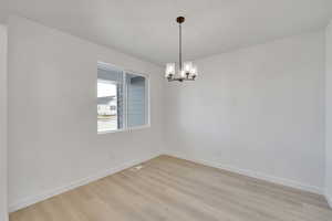 Unfurnished room featuring visible vents, light wood-style flooring, a notable chandelier, and baseboards