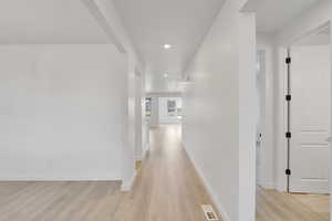 Hallway featuring light wood-style floors, baseboards, visible vents, and recessed lighting
