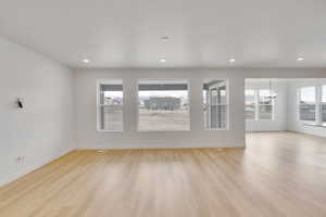 Unfurnished living room with a chandelier, light wood-type flooring, baseboards, and recessed lighting