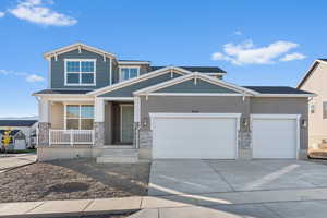 Craftsman house featuring driveway, stone siding, covered porch, and a garage