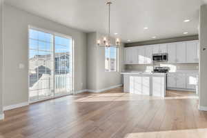 Kitchen with light wood-style floors, a notable chandelier, baseboards, and stainless steel appliances