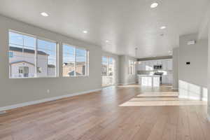 Unfurnished living room featuring light wood-style floors, recessed lighting, baseboards, and a textured ceiling