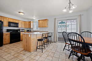 Kitchen with a kitchen bar, black appliances, a chandelier, a sink, and light countertops